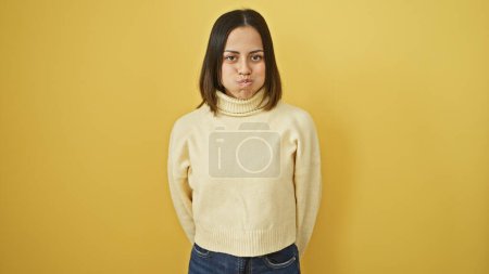 Téléchargez les photos : Portrait d'une jeune femme hispanique avec une expression ludique, portant un pull, sur un fond jaune. - en image libre de droit