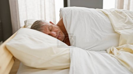 Foto de Un hombre maduro durmiendo tranquilamente en un dormitorio luminoso con sábanas blancas. - Imagen libre de derechos
