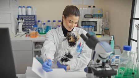 Una joven hispana examina un biewer yorkshire terrier en un laboratorio de interior.