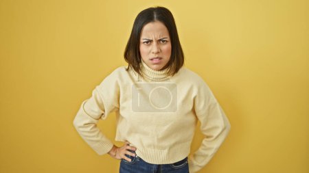 Téléchargez les photos : Jeune femme hispanique agacée avec une expression sceptique, portant un pull décontracté, se tient sur un fond jaune isolé. - en image libre de droit