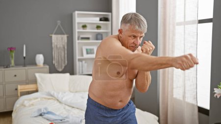 A senior man practices boxing moves in his modern bedroom, indicating a healthy, active lifestyle.