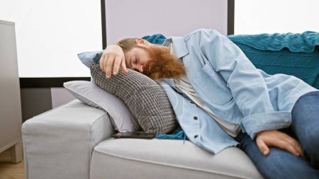 Jeune Irlandais épuisé à la barbe rousse trouve confort relaxant sur un canapé confortable, profondément dormir à la maison dans le salon, savourant la détente d'un repos bien mérité