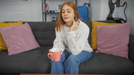 Téléchargez les photos : Jeune femme détendue profitant d'un moment confortable avec café sur un canapé confortable à la maison - en image libre de droit