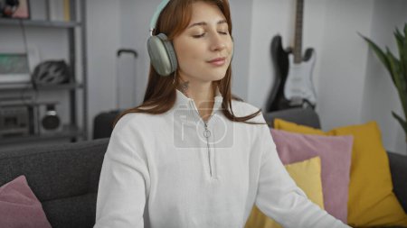 Téléchargez les photos : Une jeune femme détendue aime la musique avec écouteurs dans un confortable appartement salon. - en image libre de droit