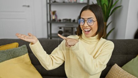 Foto de Mujer hispana sonriendo gesto presentación sala de estar gafas suéter amarillo - Imagen libre de derechos
