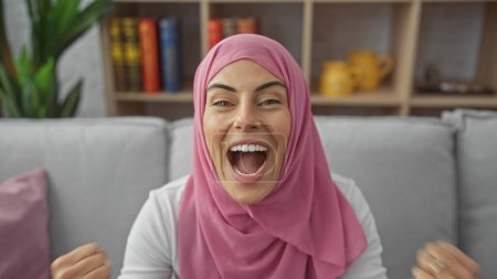 Téléchargez les photos : Femme joyeuse dans le hijab riant dans un cadre confortable salon, exsudant bonheur et positivité - en image libre de droit