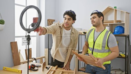 Zwei Männer arbeiten in einer hellen Tischlerei mit Werkzeug und Holzmöbeln zusammen.