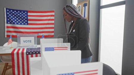 Femme afro-américaine avec des tresses votant dans une salle d'université électorale ornée de drapeaux des États-Unis