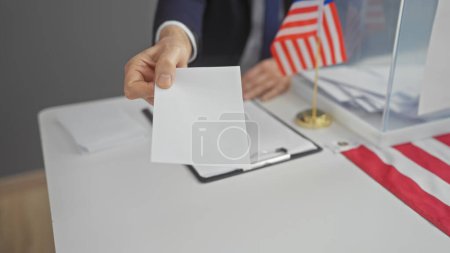Ein Mann mittleren Alters bei der Stimmabgabe in einem Wahllokal in den Vereinigten Staaten mit amerikanischer Flagge.