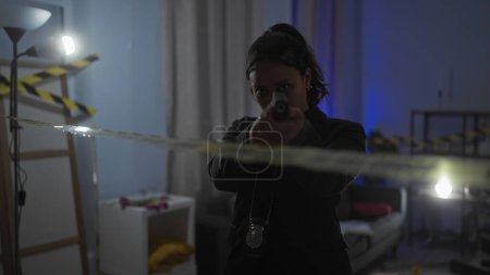 Photo for Hispanic woman detective aiming gun indoors at a crime scene with caution tape and police badge. - Royalty Free Image