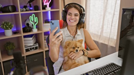 Foto de Joven mujer hispana alegre serpenteante con perro mascota se hace un selfie seguro en la sala de juegos a mitad de la corriente - Imagen libre de derechos