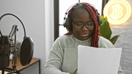 Mujer afroamericana con trenzas leyendo partituras en un estudio de radio.