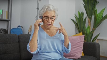 Foto de Mujer mayor usando el teléfono en una sala de estar moderna, expresando confusión - Imagen libre de derechos