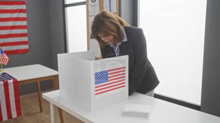 Photo for Mature woman voting in american electoral center with flag. - Royalty Free Image