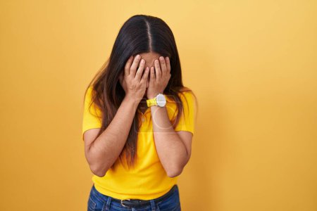Foto de Mujer árabe joven de pie sobre fondo amarillo con expresión triste cubriendo la cara con las manos mientras llora. concepto de depresión. - Imagen libre de derechos