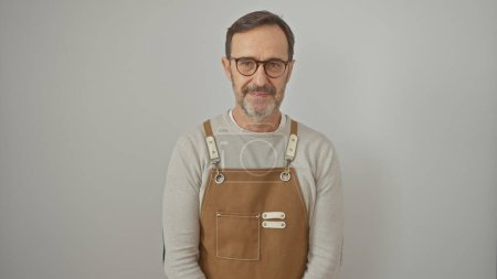 Téléchargez les photos : Un homme mûr avec des lunettes et une barbe, portant un tablier brun, pose sur un fond blanc. - en image libre de droit