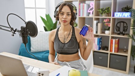 Young woman with headphones in a radio studio holding a blue pill bottle, showcasing a health segment.