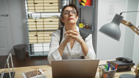 Mujer madura contemplando en la oficina con computadora portátil, evidencia, ambiente de detective y archivador