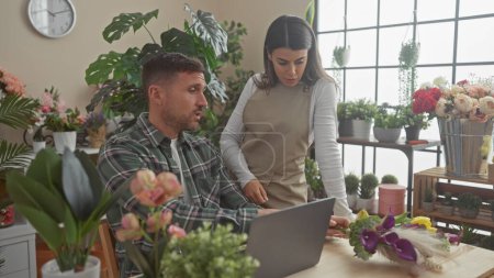 Man and woman collaborating in a flower shop surrounded by various plants, discussing work on a laptop.