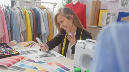 Foto de Mujer sonriente usando smartphone en un colorido estudio de diseño de moda con tela y máquina de coser - Imagen libre de derechos