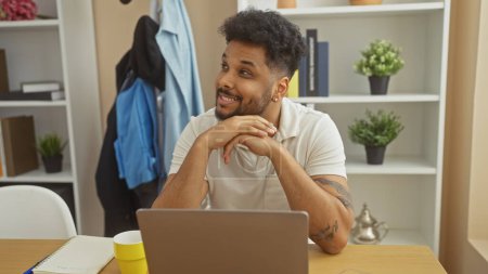 Téléchargez les photos : Smiling african american man at home office with laptop, casual, professional, modern, plants. - en image libre de droit