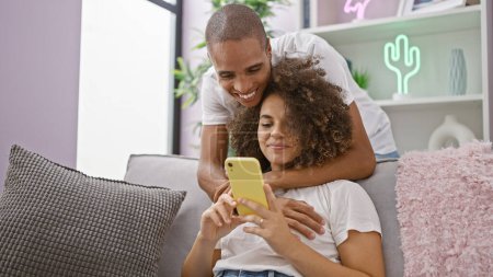 Photo for Beautiful couple confidently enjoying a fun-texting session, happily sitting on their home sofa, love radiating from their smiling expressions - Royalty Free Image