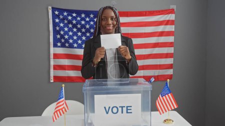 Foto de Mujer afroamericana con trenzas votando en interiores bajo bandera de estados unidos - Imagen libre de derechos