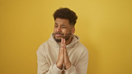 Photo for Pensive african man with closed eyes praying in casual attire against a yellow background. - Royalty Free Image