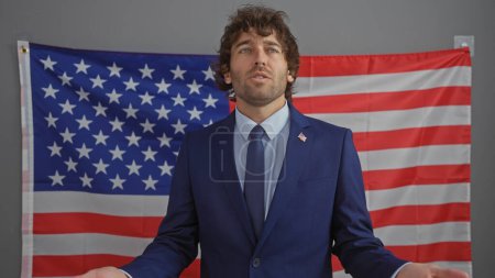 Foto de Un joven con traje se presenta ante una bandera americana, reflejando profesionalismo y patriotismo dentro de una oficina. - Imagen libre de derechos