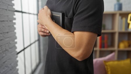 Junger hispanischer Mann mit Bart, der zu Hause eine Brieftasche in der Hand hält und einen lässigen Lebensstil in einem Innenraum präsentiert.