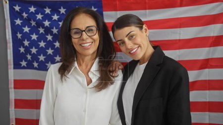 Two women smiling in an office with an american flag, portraying leadership and teamwork in the usa.