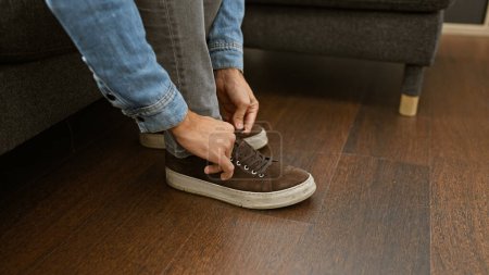 Foto de Un hombre joven se ata los zapatos en el interior, lo que implica un estilo de vida informal y el interior del hogar contemporáneo. - Imagen libre de derechos