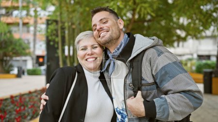 Photo for A smiling woman and man embrace each other joyfully on a city street surrounded by greenery. - Royalty Free Image