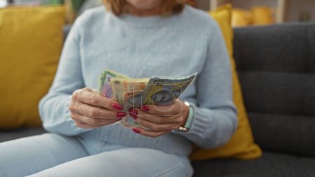Photo for Middle-aged woman counting romanian currency indoors, illustrating finance and lifestyle in a home setting. - Royalty Free Image