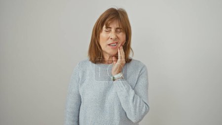 Foto de Una mujer de mediana edad experimenta dolor de muelas, sosteniendo su mejilla sobre un fondo blanco. - Imagen libre de derechos