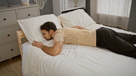 Photo for Handsome young man with a beard sleeping peacefully in a modern bedroom, depicting relaxation at home. - Royalty Free Image
