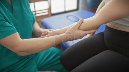 Ein Physiotherapeut im Peeling untersucht den Arm eines Patienten in einer gut beleuchteten Physiotherapie-Klinik und stellt Gesundheitswesen und Rehabilitation dar.