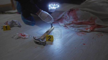 Un enquêteur judiciaire recueille des preuves sur une scène de crime intérieure ensanglantée avec un marteau, des marqueurs numérotés et des gants.