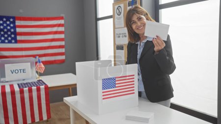 Foto de Mujer madura sonriendo mientras vota en las elecciones americanas, banderas y urnas visibles. - Imagen libre de derechos