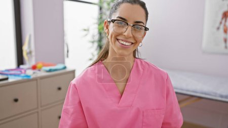 Téléchargez les photos : Jeune femme hispanique confiante et souriante, une belle thérapeute appréciant son travail en physiothérapie avec une expression heureuse dans une clinique de désintox - en image libre de droit