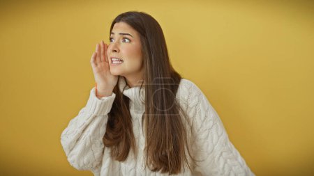 Foto de Una joven con el pelo largo y morena grita algo sobre un fondo amarillo aislado, retratando expresividad y dinamismo. - Imagen libre de derechos
