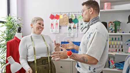 Téléchargez les photos : Deux tailleurs, une femme et un homme, conversent joyeusement dans une boutique de tailleurs vibrante remplie de croquis de mode et d'équipements de couture. - en image libre de droit