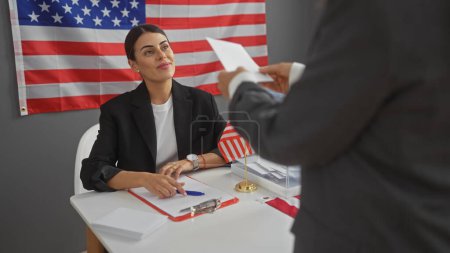 Candidate woman and man in suit indoors with united states flag, discussing papers during electoral event.