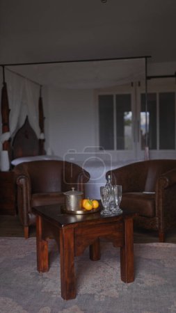 Photo for Elegant interior with vintage leather sofa, wooden table, silver teapot, glassware, and oranges. - Royalty Free Image