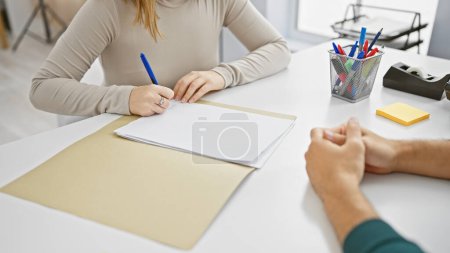 Photo for Man and woman engage in discussion at a white table in a modern office setup, with office supplies and paperwork. - Royalty Free Image