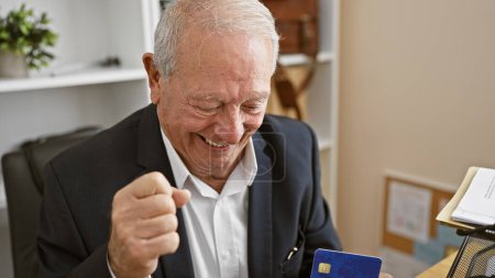 Téléchargez les photos : Joyeux travailleur senior célébrant le succès de l'entreprise par carte de crédit au bureau - en image libre de droit