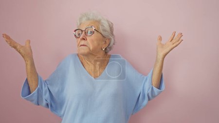A perplexed senior woman with gray hair and glasses gesturing uncertainty against a pink background.