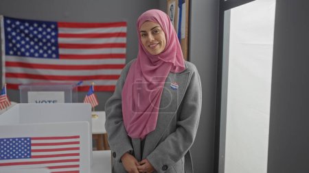 Téléchargez les photos : Une belle hispanique portant un hijab sourit dans un centre de vote américain avec des drapeaux. - en image libre de droit