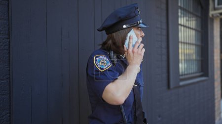 Mature woman police officer in uniform talking on phone outdoors in urban setting.