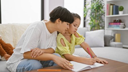 Photo for Relishing mother-daughter bond, sitting together at home, drawing intimate expressions on notebook in the quietude of their living room - Royalty Free Image